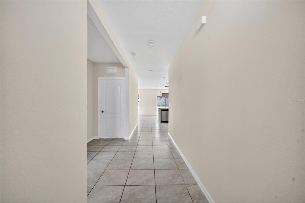 A hallway with light-colored walls and gray tiled flooring leads toward an open kitchen area — 265 MEADOWBROOK BOULEVARD, WINTER HAVEN, FL
