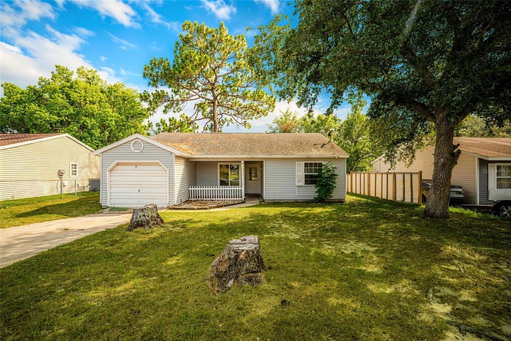 A single-story house with light gray siding, a garage, and two tree stumps in front — 21 SPRING LOOP CIRCLE, OCALA, FL