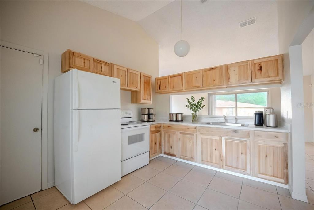 A kitchen features light wood cabinets, white appliances, tile flooring, and a vaulted ceiling — 21 SPRING LOOP CIRCLE, OCALA, FL
