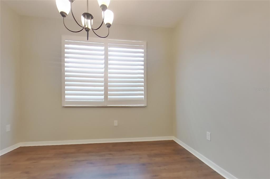 An empty dining room features light-colored walls, wood-look flooring, a window with shutters, and a chandelier — 1255 MERION DRIVE, MOUNT DORA, FL