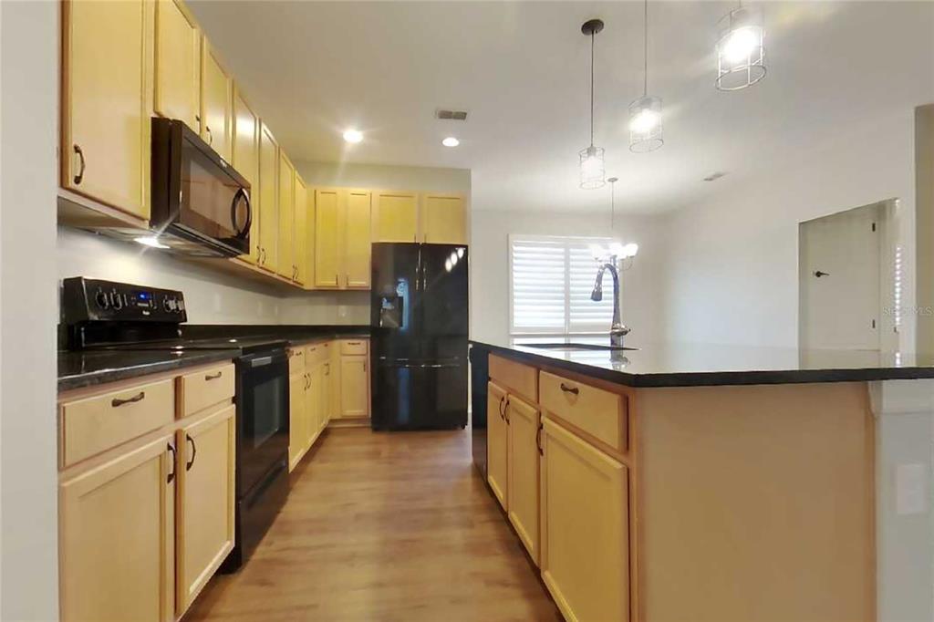 A kitchen features light wood cabinets, black appliances, a granite island, and pendant lighting — 1255 MERION DRIVE, MOUNT DORA, FL