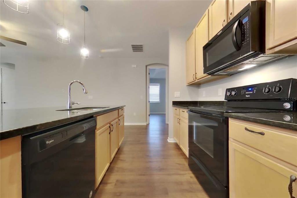 A kitchen features light wood cabinets, black appliances, dark countertops, and wood-look flooring — 1255 MERION DRIVE, MOUNT DORA, FL