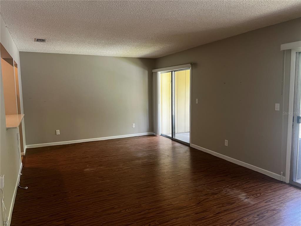 An empty living room features dark wood-look flooring, beige walls, and a sliding glass door — 140 ORCHID WOODS COURT UNIT 15B, DELTONA, FL