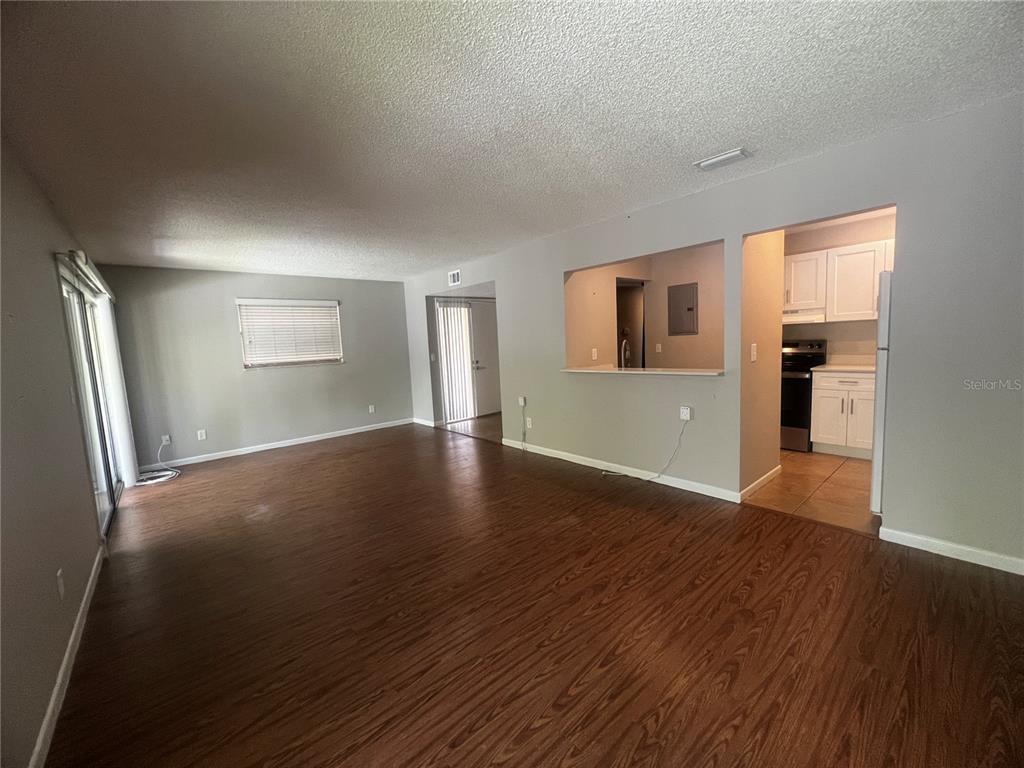 An open-concept living room with wood-look flooring leads to a kitchen with white cabinets — 140 ORCHID WOODS COURT UNIT 15B, DELTONA, FL