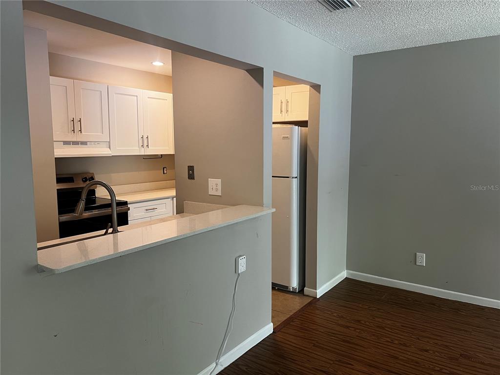 A kitchen with white cabinets and a breakfast bar overlooks a room with wood flooring — 140 ORCHID WOODS COURT UNIT 15B, DELTONA, FL