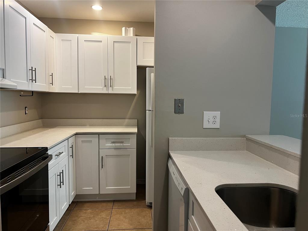A kitchen features white cabinets, light countertops, a refrigerator, and a stainless steel sink — 140 ORCHID WOODS COURT UNIT 15B, DELTONA, FL