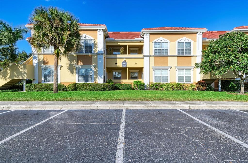 A two-story apartment building with a tiled roof, stucco exterior, and a parking lot foreground — 3005 CHIANTI COURT UNIT 103, SARASOTA, FL