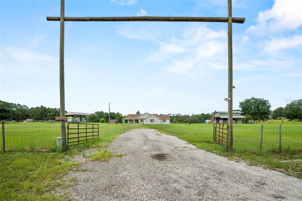 A gravel driveway leads through a wooden gate toward a house and outbuildings on land — 41636 OUTLAW LANE, WEIRSDALE, FL