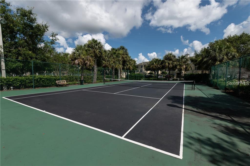 A fenced outdoor tennis court with a black surface and green surrounding area — 18489 BRIDLE CLUB DRIVE UNIT 184k, TAMPA, FL