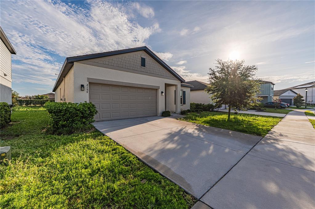 A single-story suburban house with a tan stucco exterior, a two-car garage, and a driveway — 2154 DERWENT DRIVE, DAVENPORT, FL