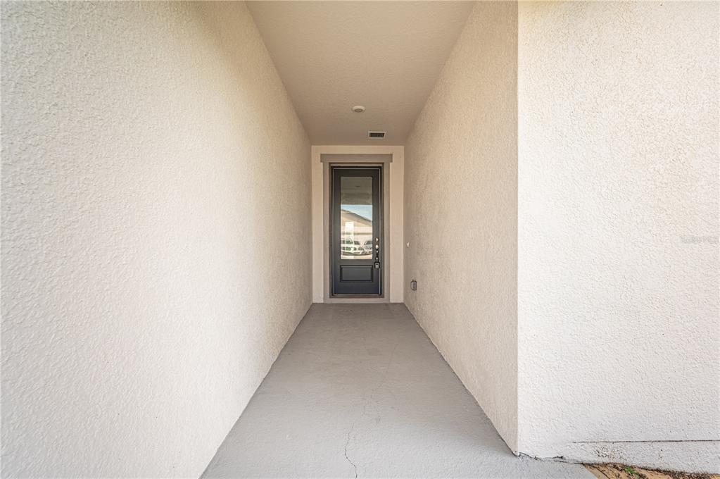 A covered entryway features a gray concrete floor, stucco walls, and a glass-paneled front door — 2154 DERWENT DRIVE, DAVENPORT, FL