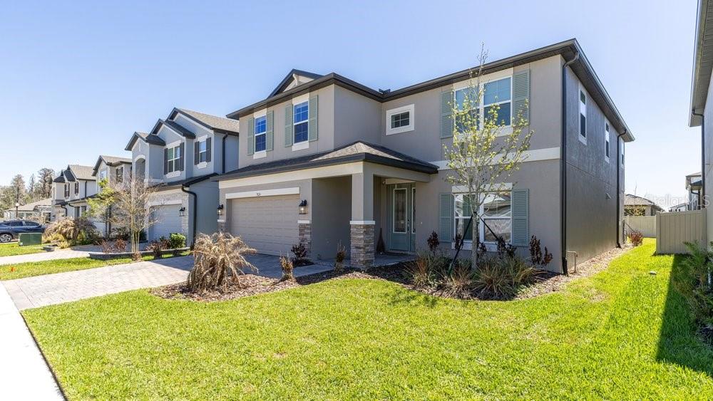 A two-story suburban house with a gray exterior, stone accents, and a two-car garage — 7824 NOTCHED PINE BEND, WESLEY CHAPEL, FL