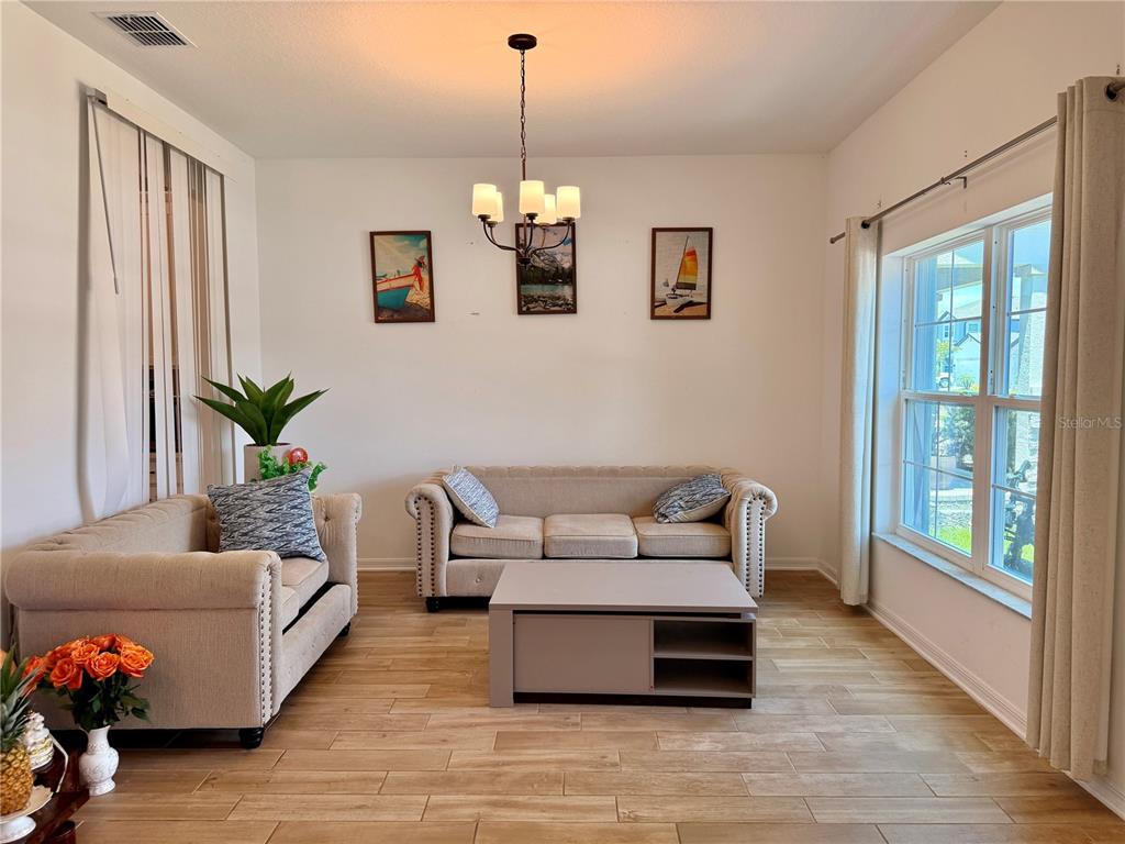 A living room features beige sofas, a coffee table, and three framed pictures on walls — 7824 NOTCHED PINE BEND, WESLEY CHAPEL, FL