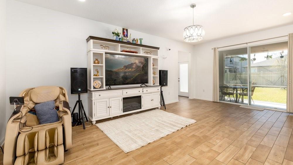 A living room features light wood-look tile floors, a white entertainment center, and a massage chair — 7824 NOTCHED PINE BEND, WESLEY CHAPEL, FL