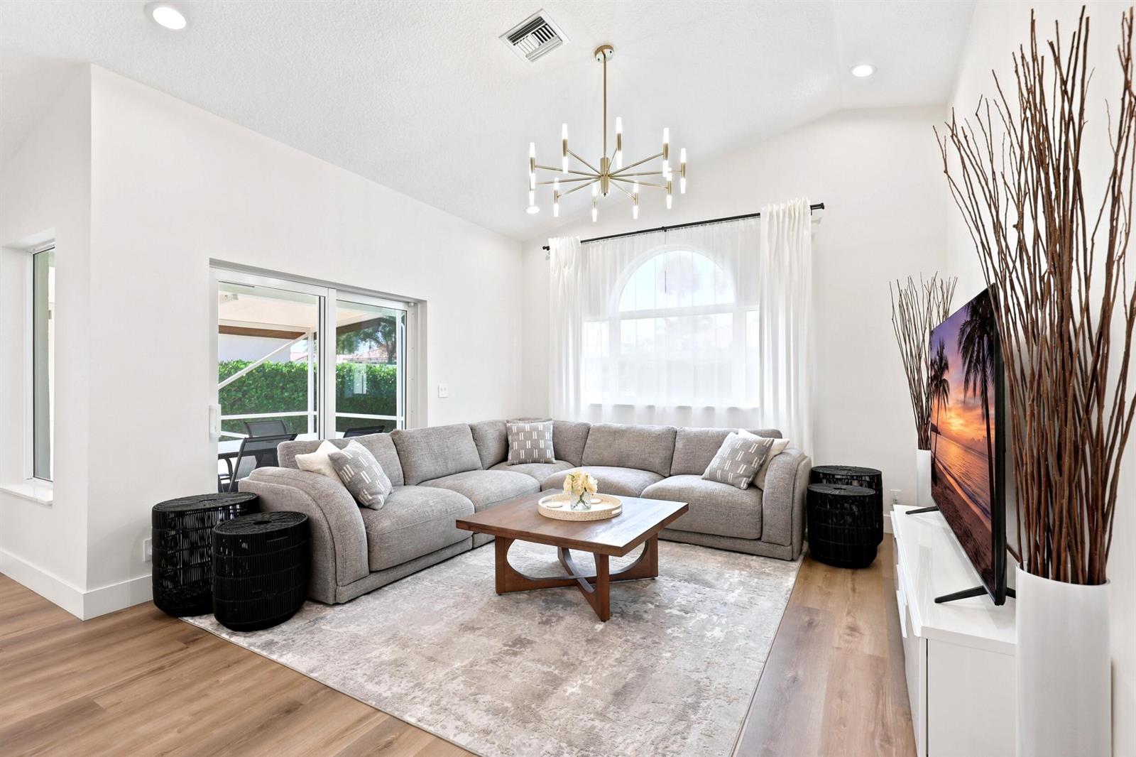 A living room features a grey sectional sofa, a wooden coffee table, and a modern chandelier — 5212 Bodega Place, Delray Beach FL 33484, DELRAY BEACH, FL