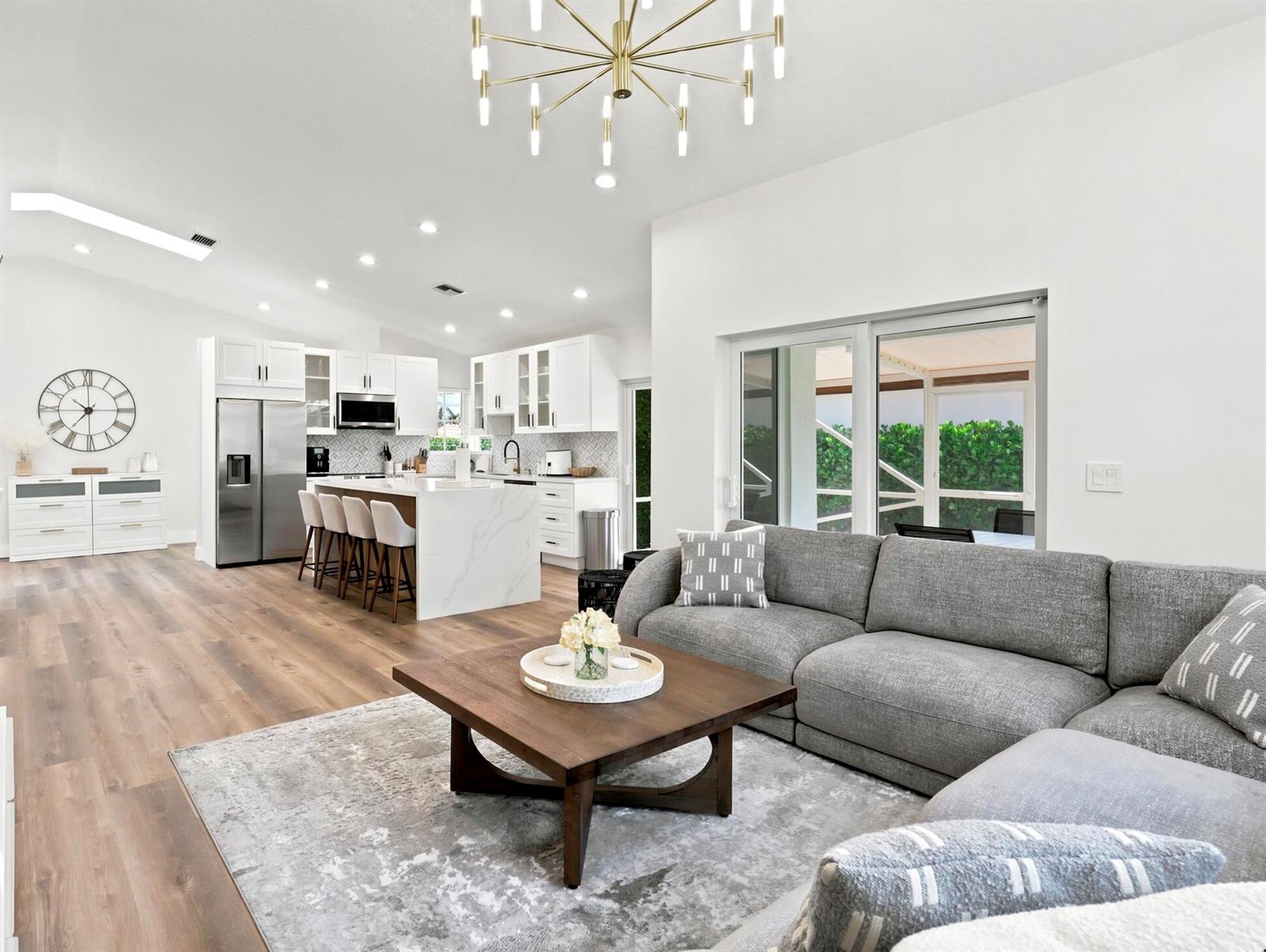 An open-concept living room and kitchen feature white cabinetry, a large island, and wood flooring — 5212 Bodega Place, Delray Beach FL 33484, DELRAY BEACH, FL