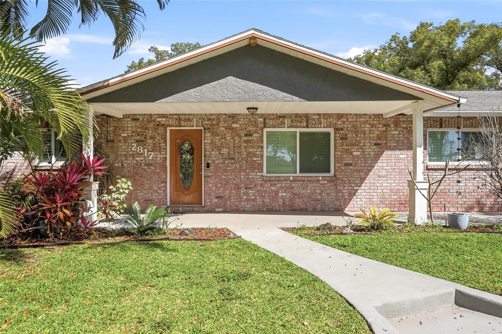 A single-story brick house features a covered front porch, a wooden door, and green lawn — 2817 FLEEMAN ROAD, PALM HARBOR, FL
