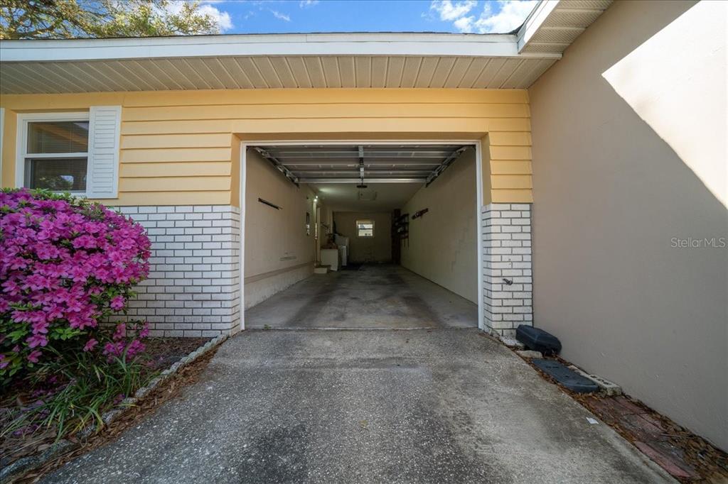 An open garage with a concrete floor and white brick accents sits beside a flowering bush — 8702 SW 94TH STREET UNIT A, OCALA, FL