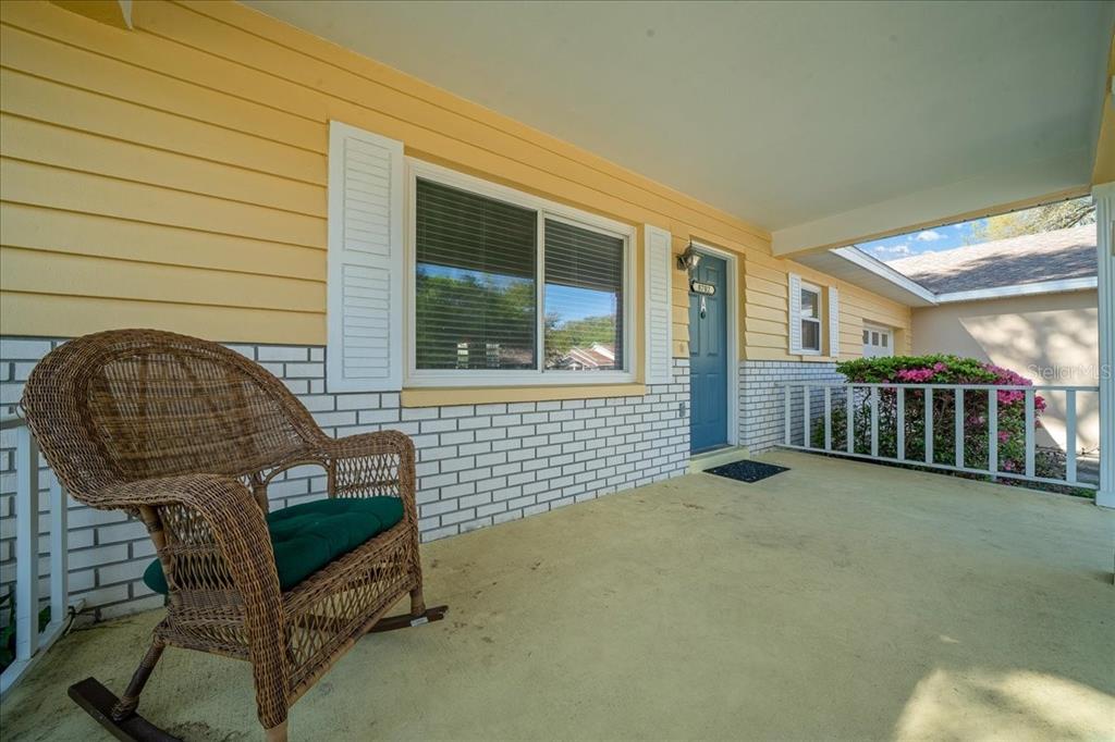 A covered front porch features a wicker rocking chair, yellow siding, and white brick accents — 8702 SW 94TH STREET UNIT A, OCALA, FL