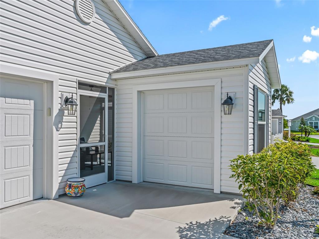 A white house exterior features a garage, a screen door, and a small concrete patio — 7536 KUENHER COURT, THE VILLAGES, FL