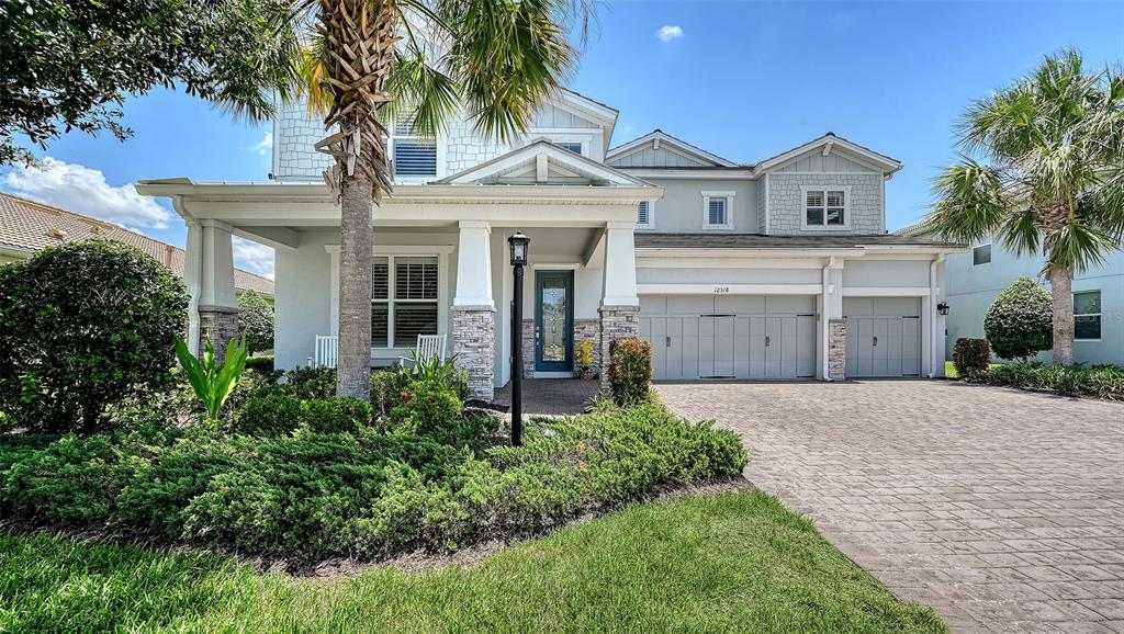 A two-story house features a covered front porch, stone accents, and a paved driveway — 12318 BLUE HILL TRAIL, BRADENTON, FL