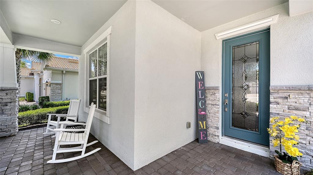 A covered front porch features a teal door, two white rocking chairs, and stone accents — 12318 BLUE HILL TRAIL, BRADENTON, FL