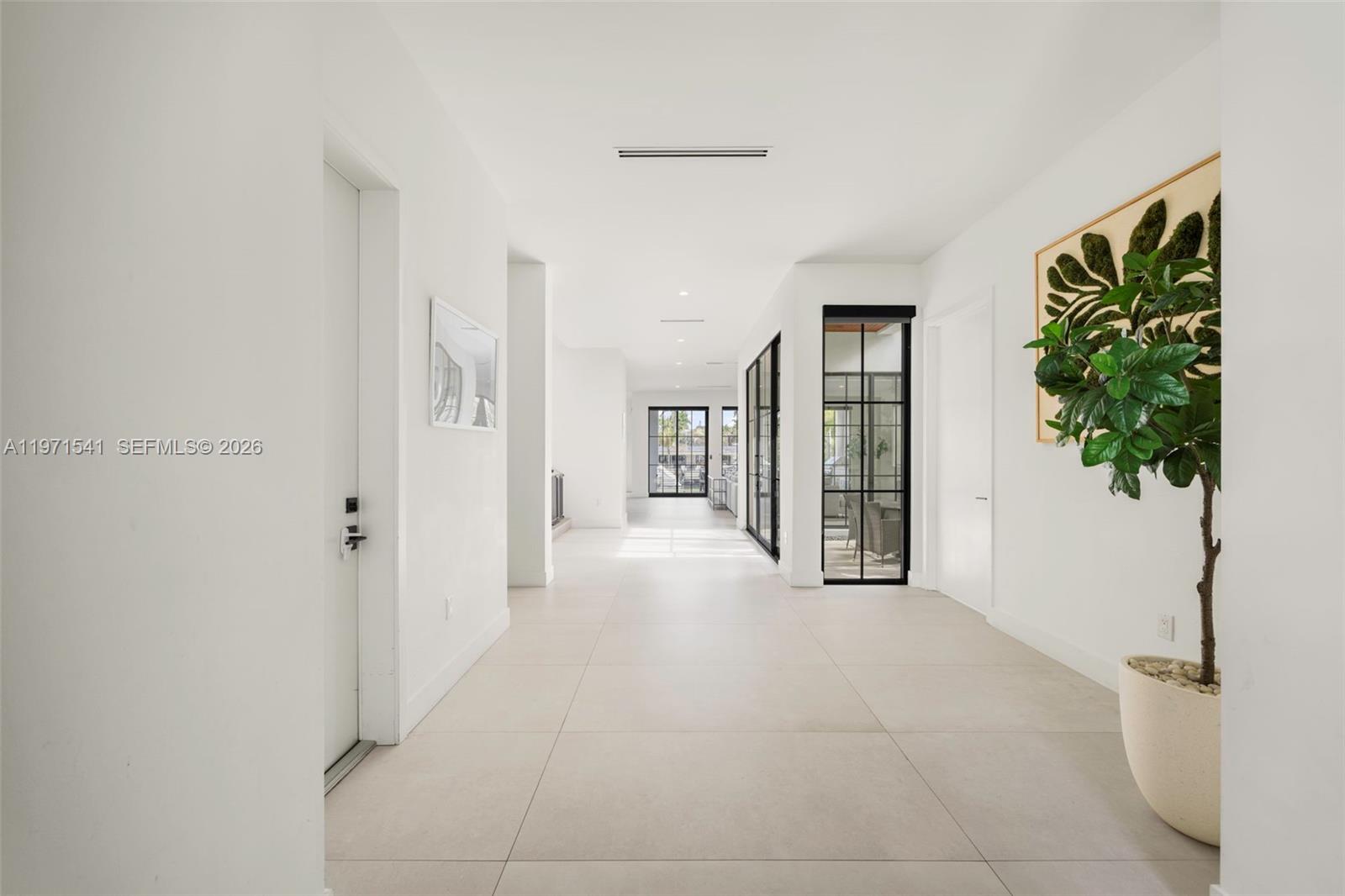 A bright, minimalist hallway features white walls, large light-colored floor tiles, and black-framed glass doors — 885 NE 76th St, Miami FL 33138, MIAMI, FL