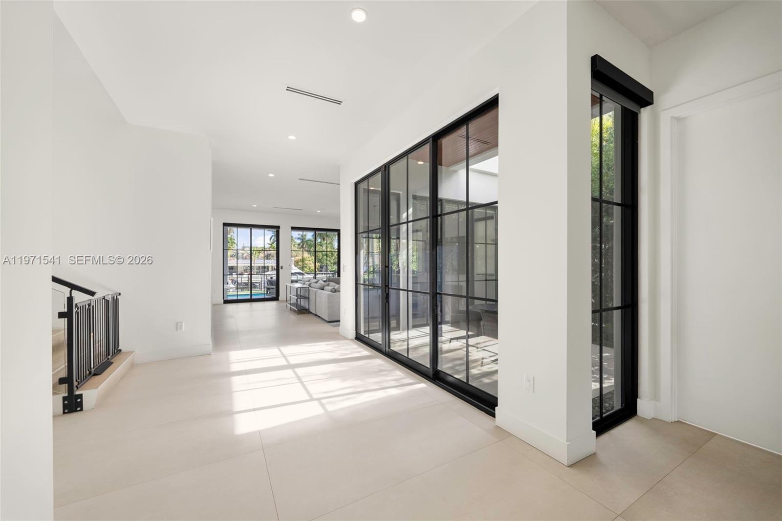 A bright, minimalist hallway features large black-framed glass doors and light-colored tile flooring — 885 NE 76th St, Miami FL 33138, MIAMI, FL