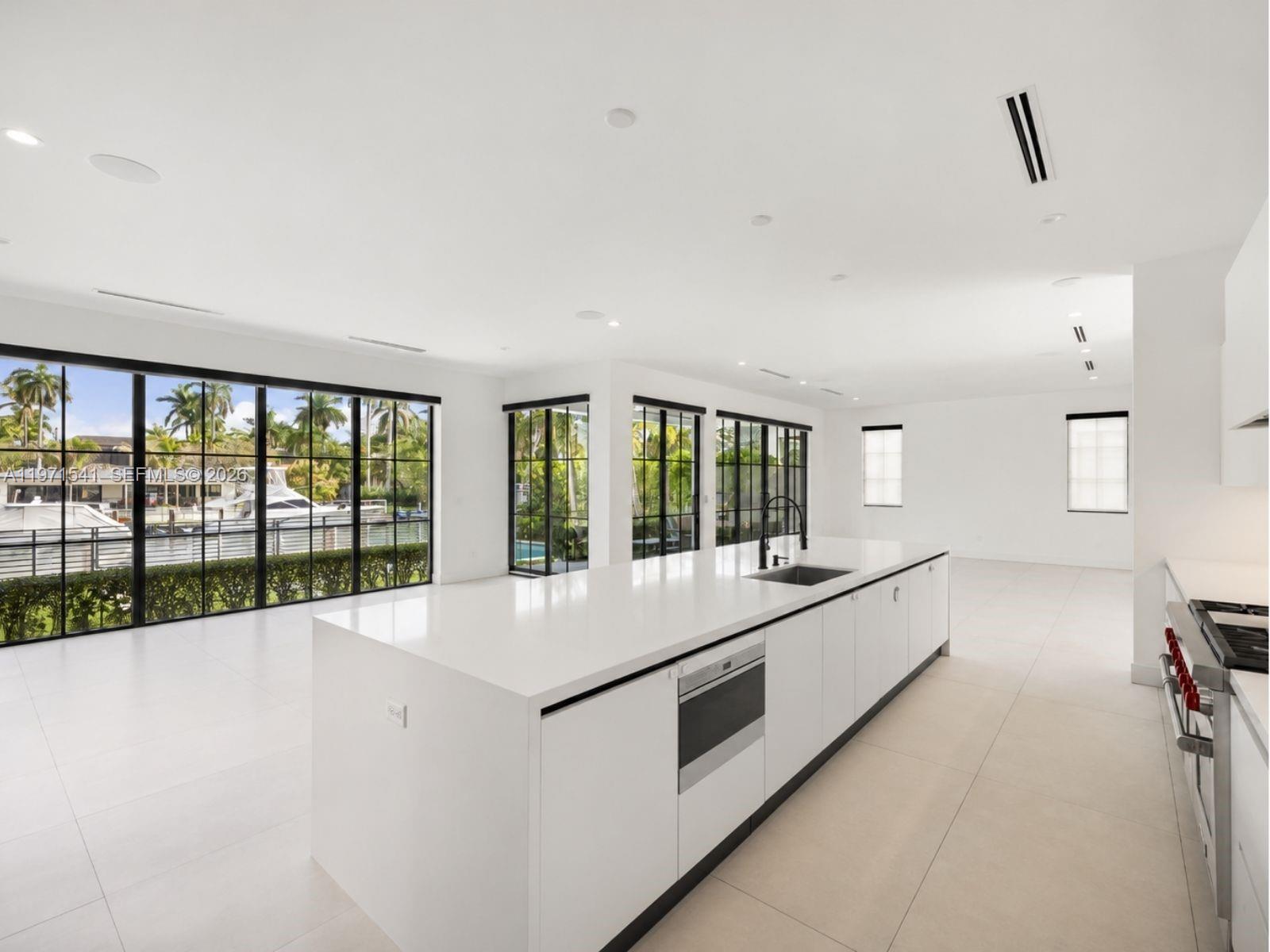 A modern white kitchen features a large center island, stainless steel appliances, and floor-to-ceiling windows — 885 NE 76th St, Miami FL 33138, MIAMI, FL