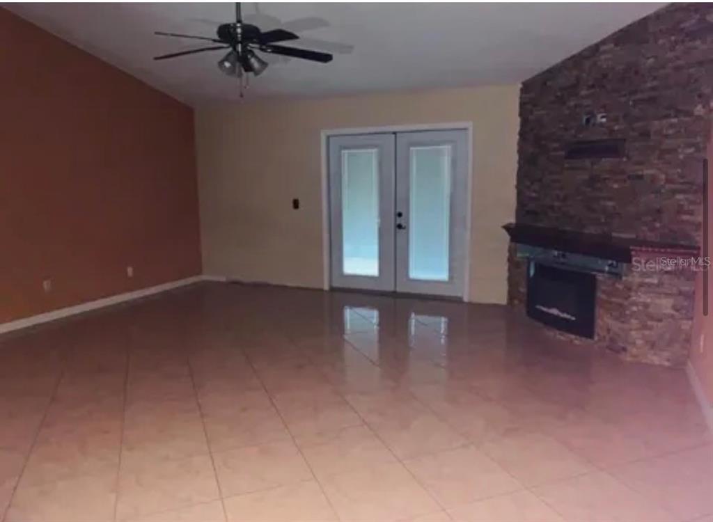 A living room features tile flooring, a stone fireplace, and double glass doors — 704 CARACARA COURT, KISSIMMEE, FL