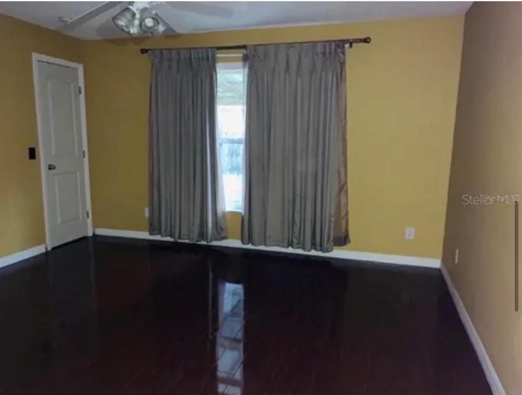 A bedroom with dark hardwood floors, mustard-colored walls, and floor-length curtains over a window — 704 CARACARA COURT, KISSIMMEE, FL
