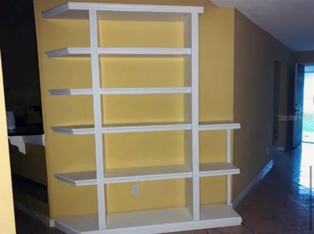 A white built-in bookshelf with multiple shelves stands against a yellow wall in a room — 704 CARACARA COURT, KISSIMMEE, FL