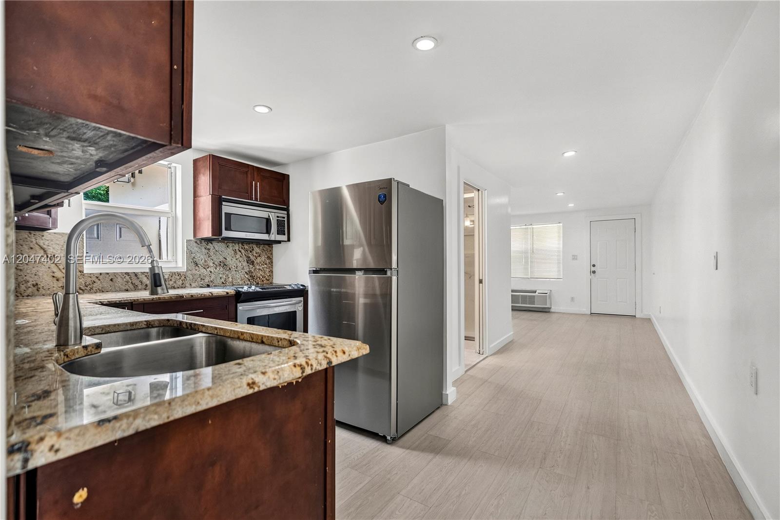 A kitchen with granite countertops and stainless steel appliances opens into a living area — 5800 Taylor St # 2, Hollywood FL 33021, HOLLYWOOD, FL