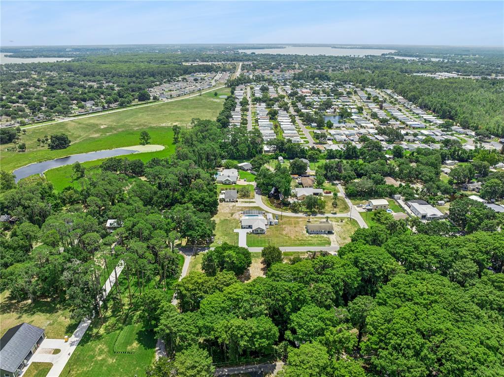 An aerial view shows a residential neighborhood with houses, dense trees, and a small pond — COVE ROAD, TAVARES, FL