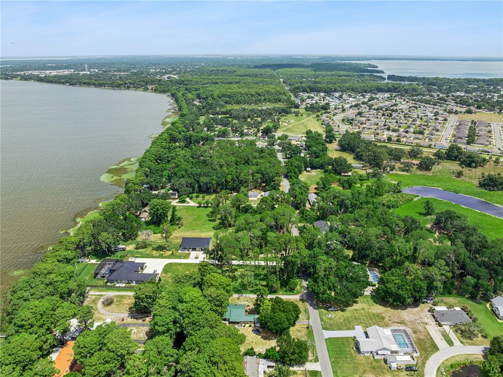 An aerial view shows a residential area with houses, dense trees, and a large lake — COVE ROAD, TAVARES, FL