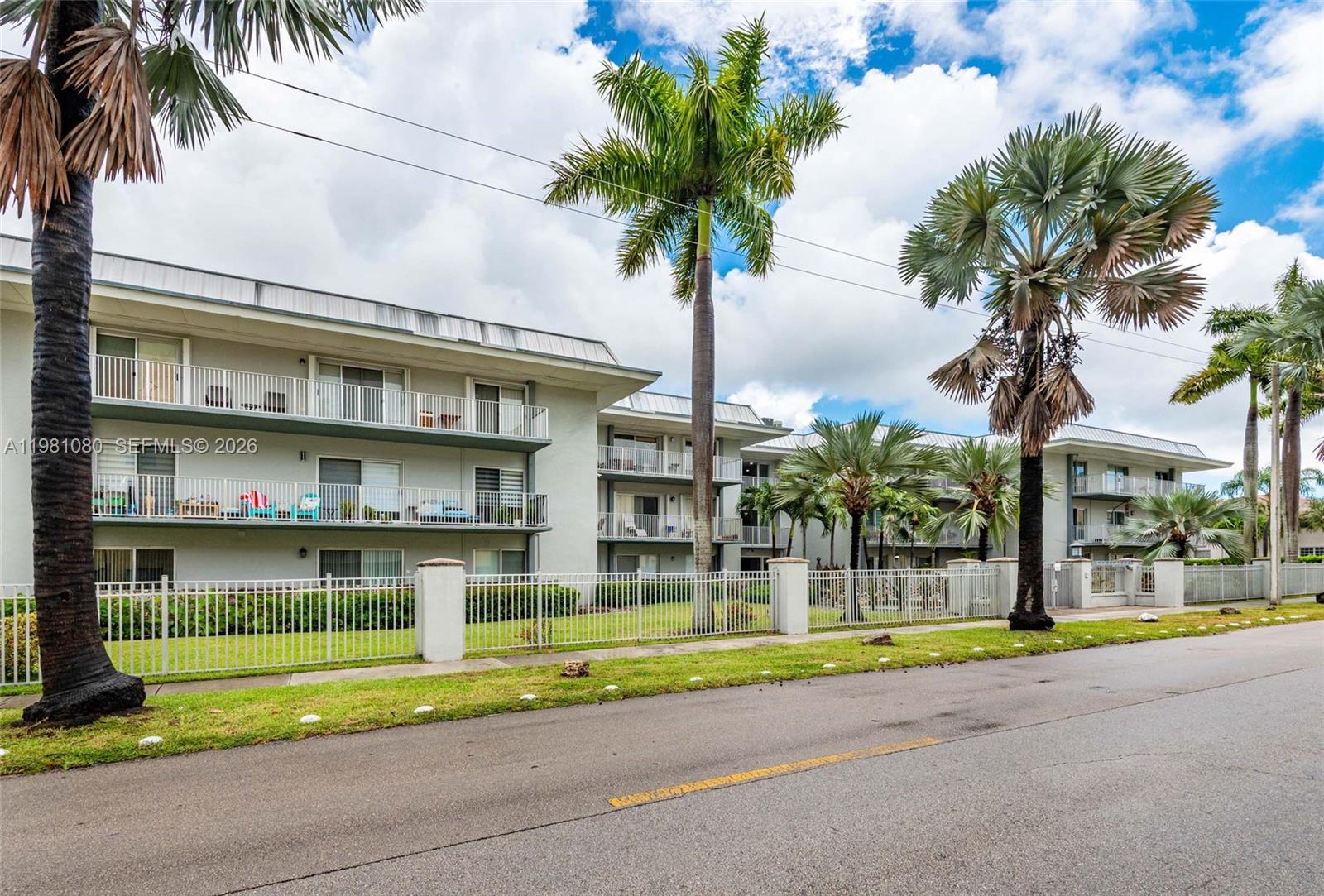 A three-story apartment building with balconies is viewed from a street behind a fence — 7403 SW 82nd St # 212N, Miami FL 33143, MIAMI, FL