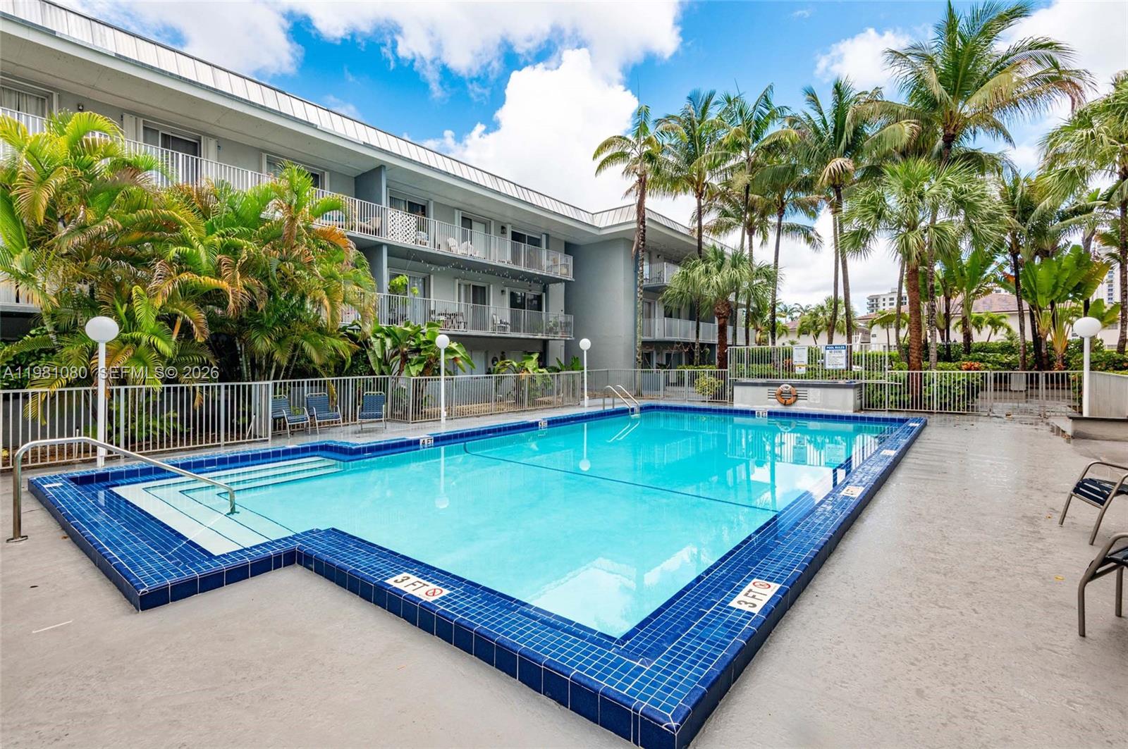 A rectangular swimming pool with blue tile borders sits in front of a multi-story apartment building — 7403 SW 82nd St # 212N, Miami FL 33143, MIAMI, FL