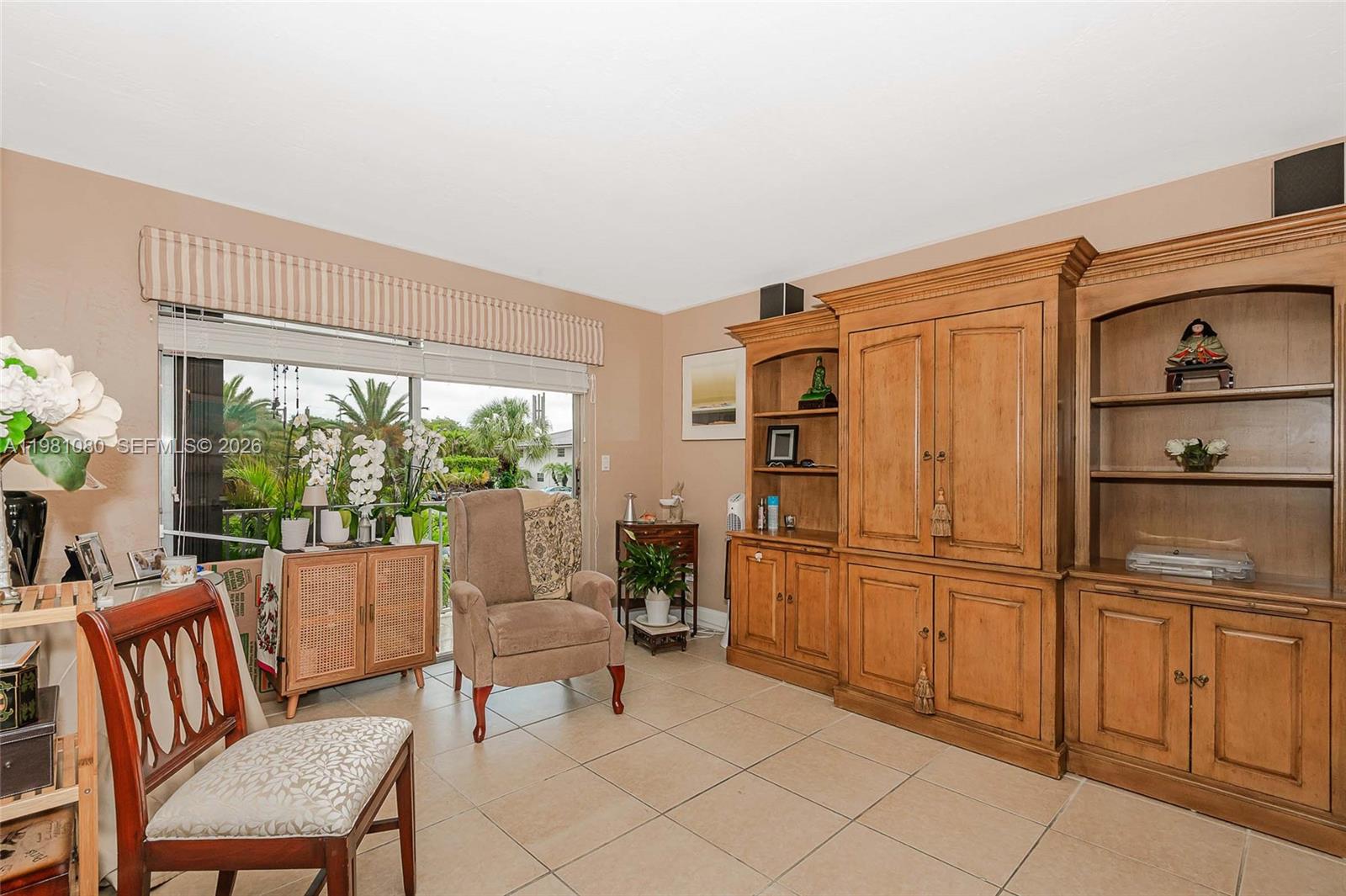 A living room features tile flooring, a large wooden wall unit, and a window with blinds — 7403 SW 82nd St # 212N, Miami FL 33143, MIAMI, FL