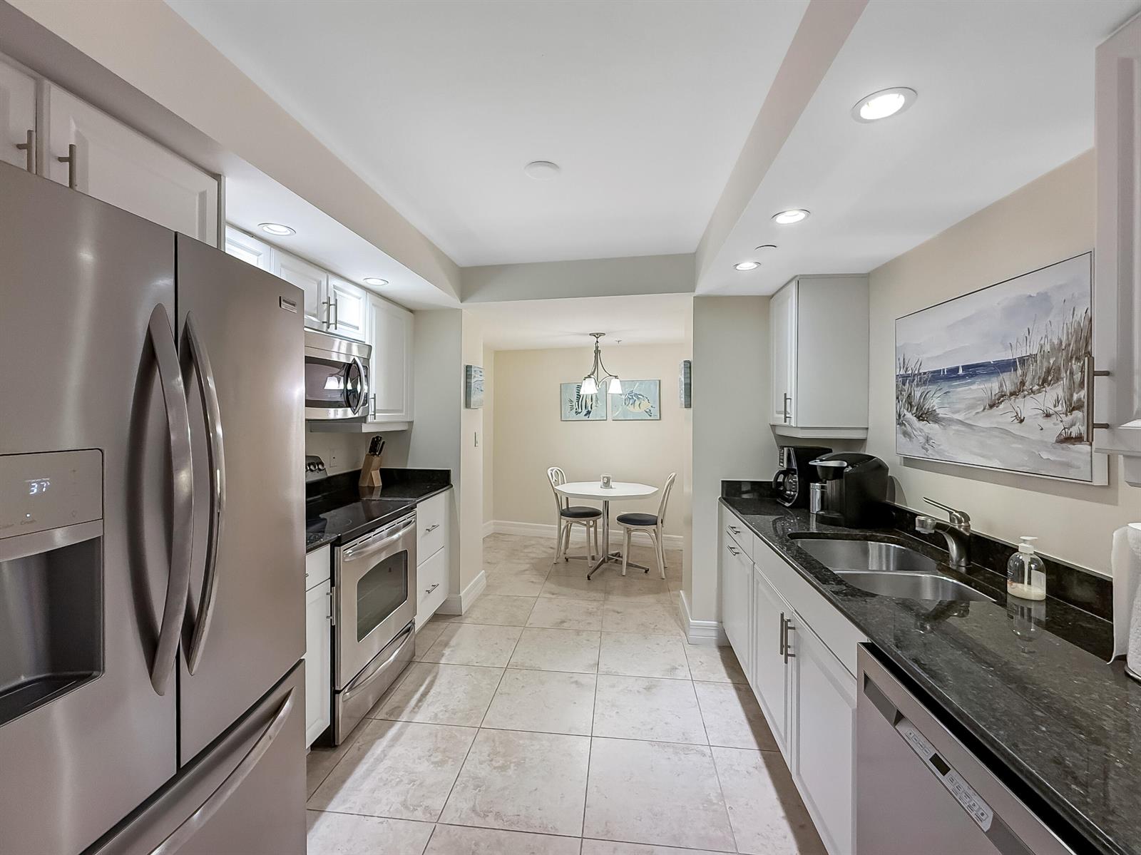 A galley kitchen features white cabinets, black granite countertops, stainless steel appliances, and tile flooring — 3000 N Ocean Drive, Singer Island FL 33404, SINGER ISLAND, FL