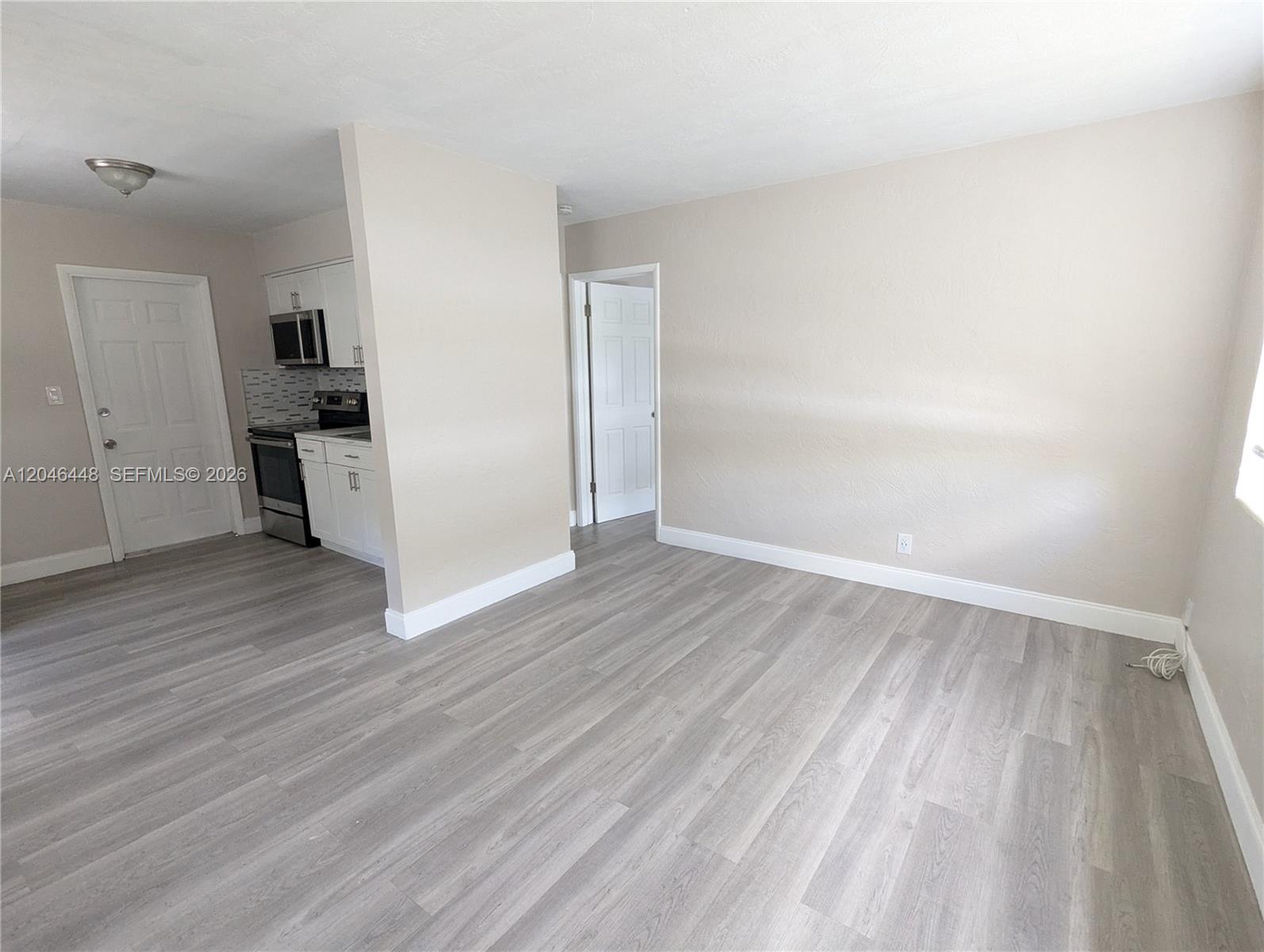 An interior view shows a living area with light wood flooring and an adjacent kitchen — 2300 Douglas St # 1, Hollywood FL 33020, HOLLYWOOD, FL