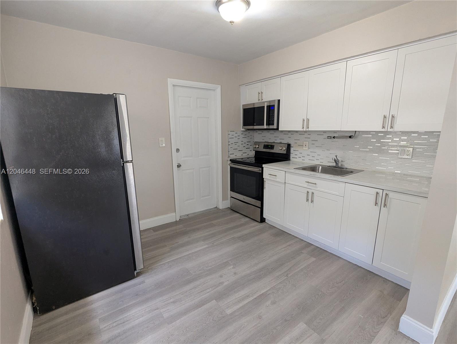A kitchen features white cabinets, stainless steel appliances, a tiled backsplash, and light wood flooring — 2300 Douglas St # 1, Hollywood FL 33020, HOLLYWOOD, FL