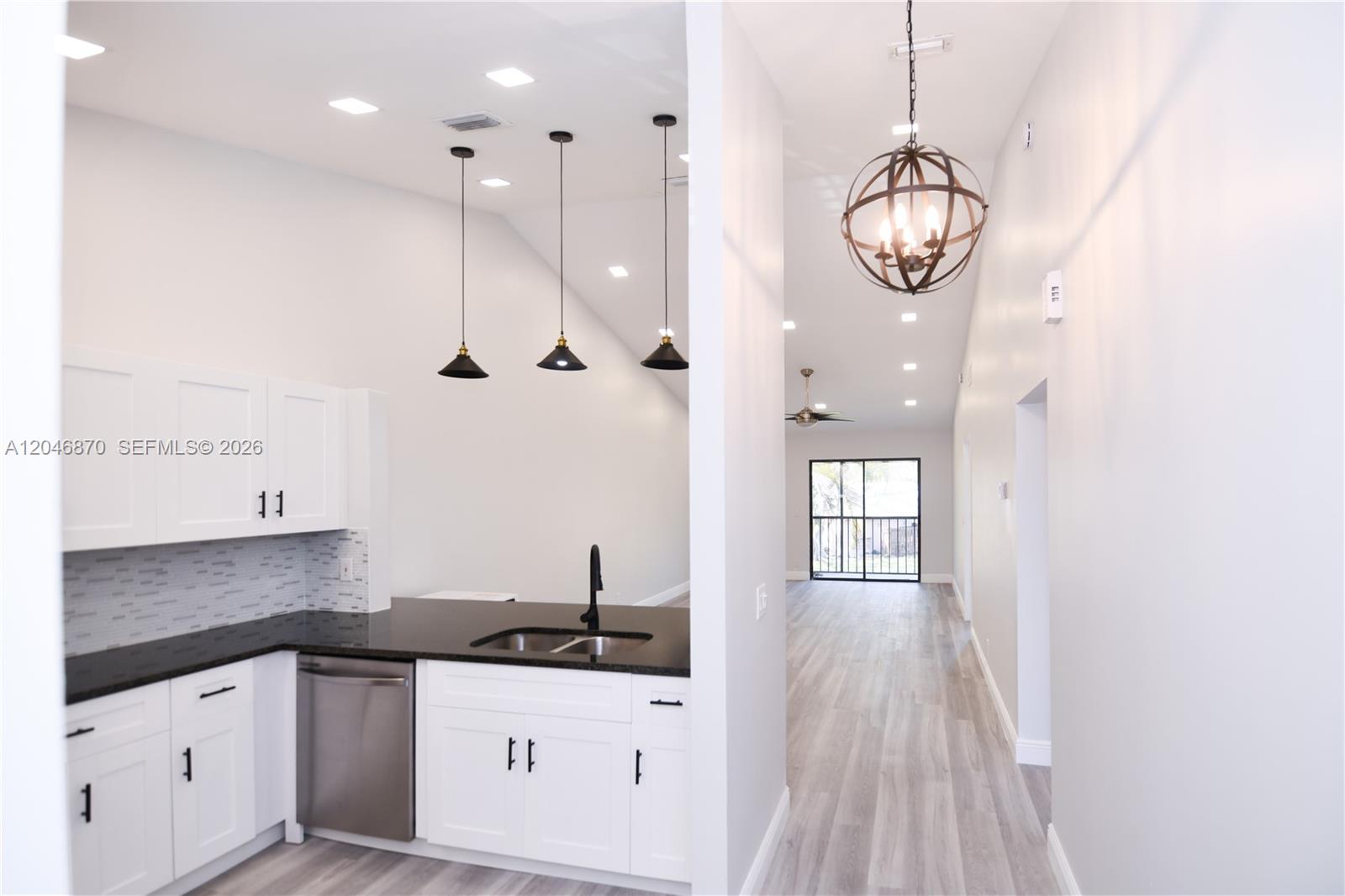 A kitchen with white cabinets and black countertops opens into a bright, vaulted-ceiling living area — 2315 SW 22nd Ave # 2020, Delray Beach FL 33445, DELRAY BEACH, FL