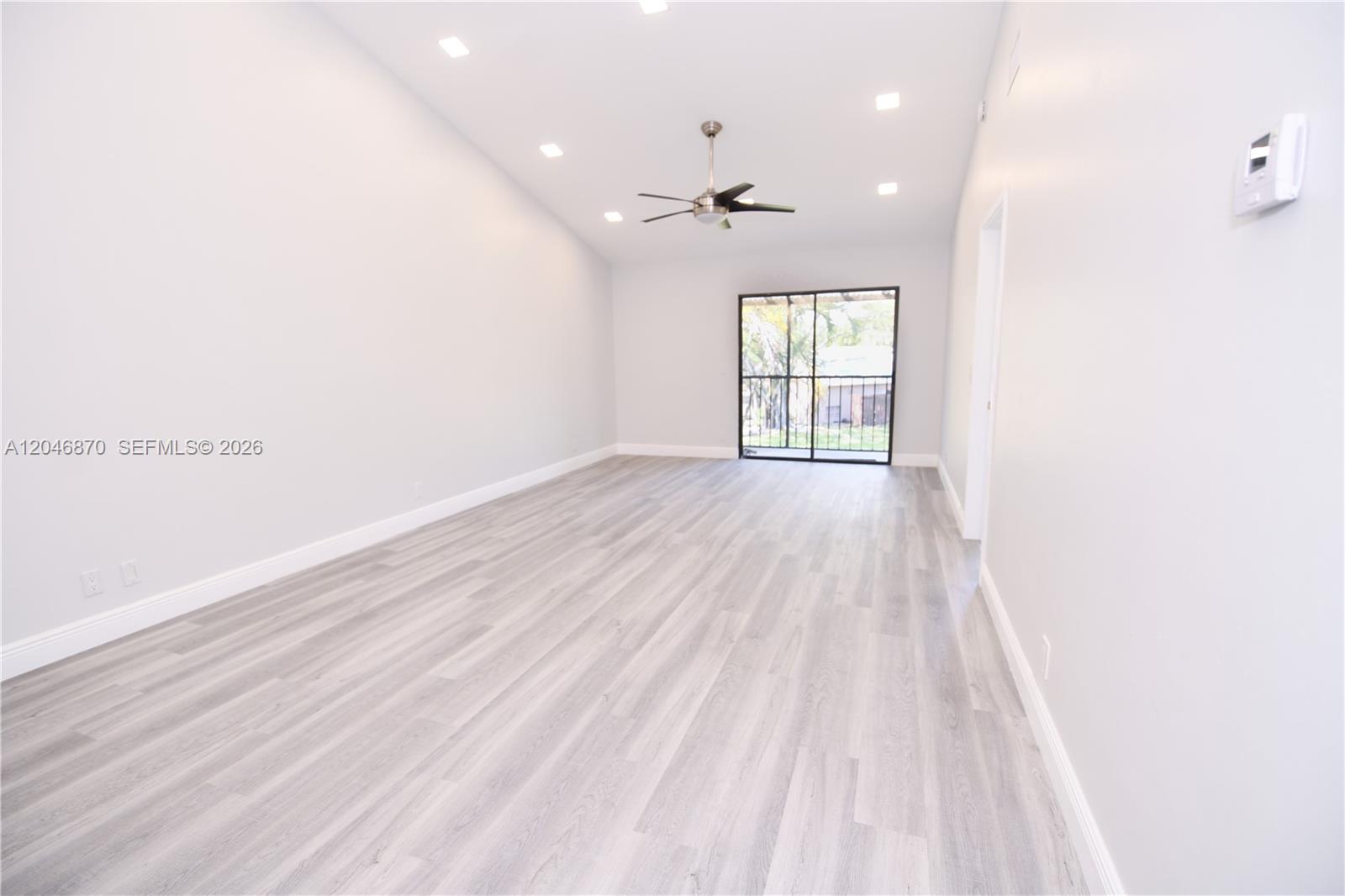 A spacious, empty room features light gray wood-look flooring, recessed lighting, and a sliding glass door — 2315 SW 22nd Ave # 2020, Delray Beach FL 33445, DELRAY BEACH, FL