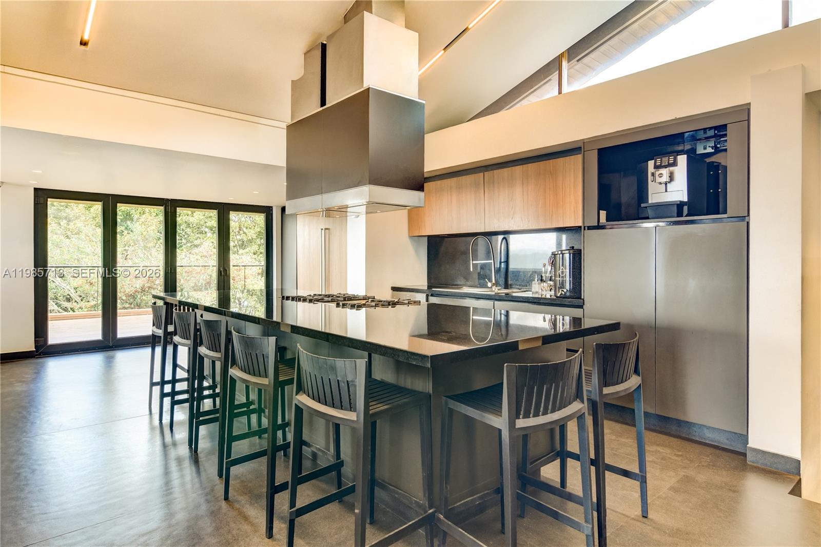 A modern kitchen features a large black island with bar stools and stainless steel appliances — 2 Vía Chía Condominio Sindamanoy, FL, FL