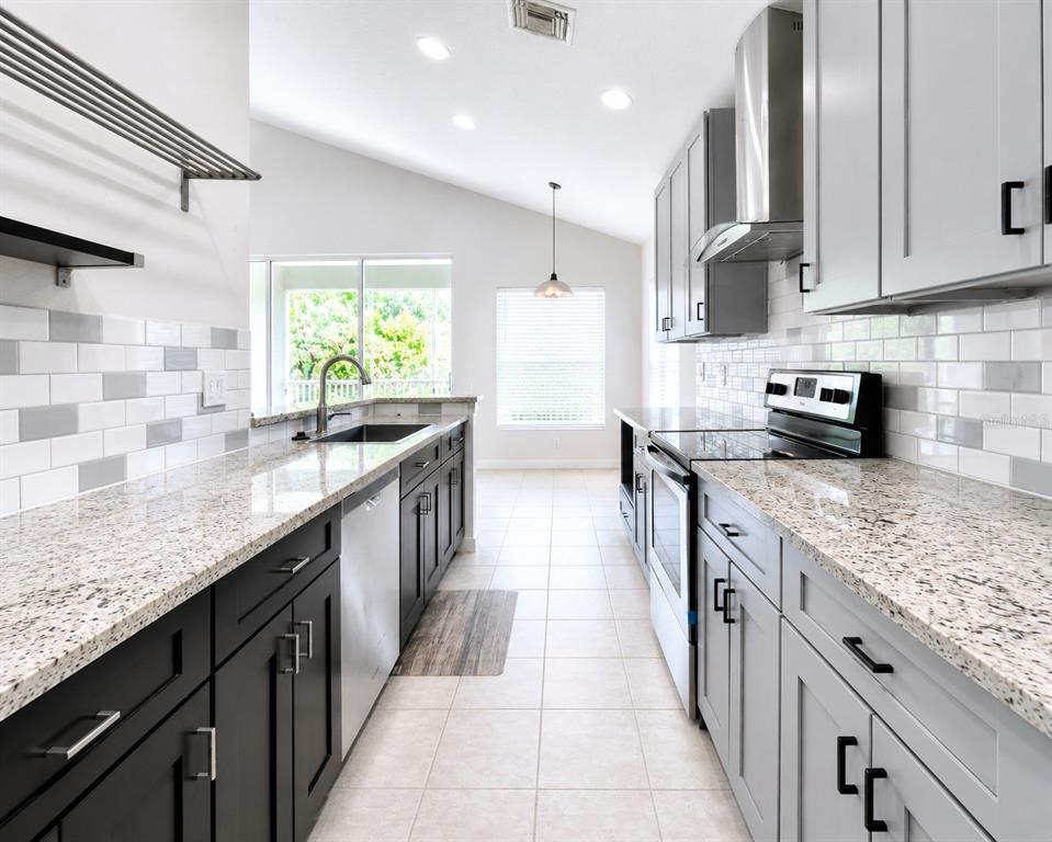 A galley kitchen features dark lower cabinets, light upper cabinets, granite countertops, and a subway tile backsplash — 2096 KINGS PALACE DRIVE, RIVERVIEW, FL