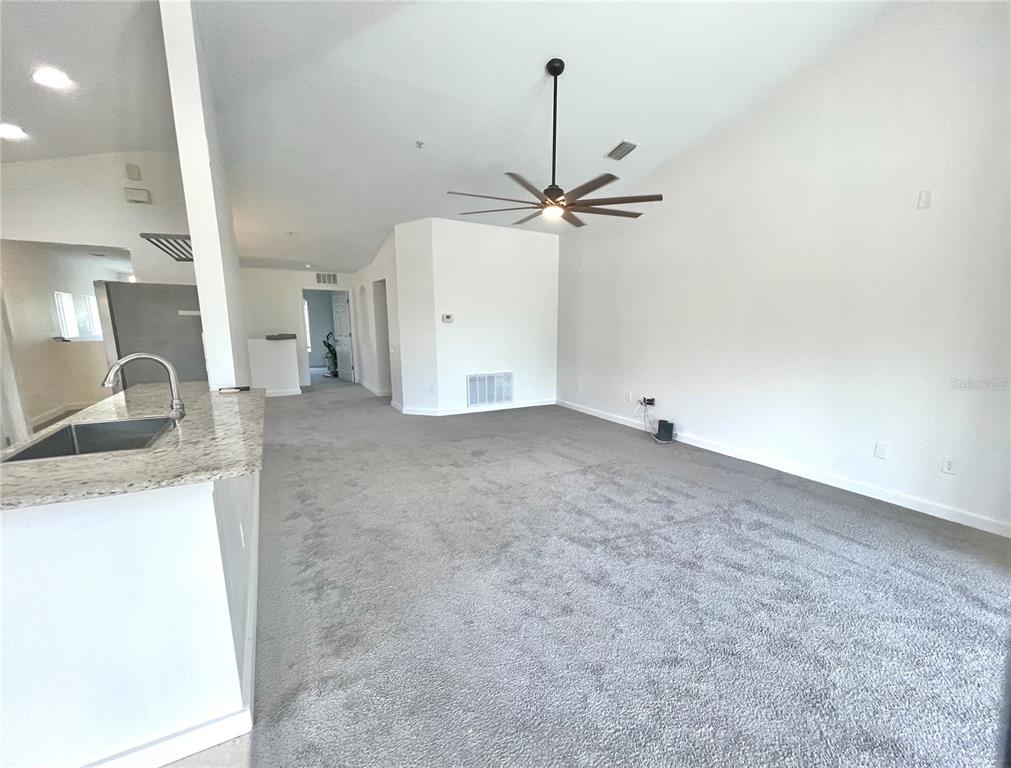 A carpeted living room features a ceiling fan and an open view of the kitchen — 2096 KINGS PALACE DRIVE, RIVERVIEW, FL