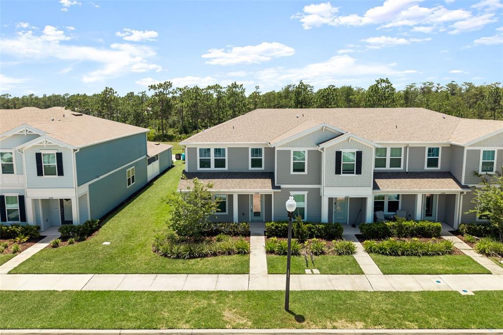 An aerial view shows the front exteriors of two multi-story suburban townhomes with landscaped yards — 5592 PINELAND RUN, ORLANDO, FL