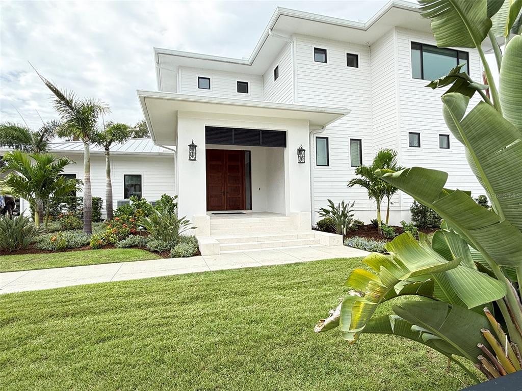 A white two-story house features a covered entryway with double wood doors and tropical landscaping — 101 DUE EAST STREET, NEW SMYRNA BEACH, FL