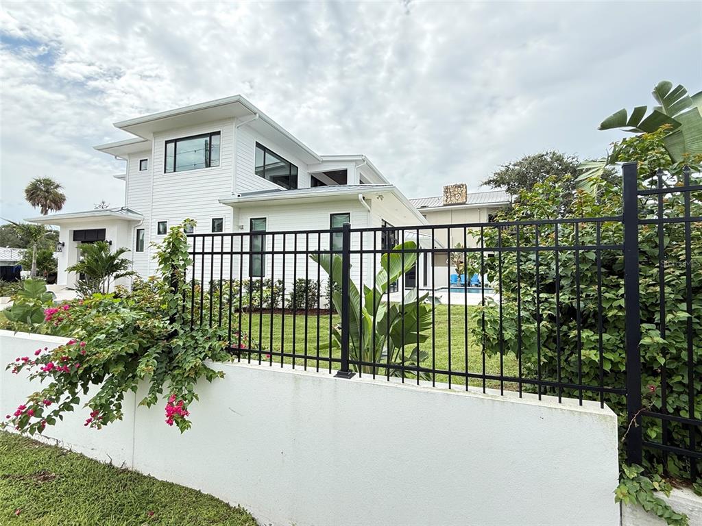 A white modern house with a black metal fence and blooming bougainvillea in the foreground — 101 DUE EAST STREET, NEW SMYRNA BEACH, FL
