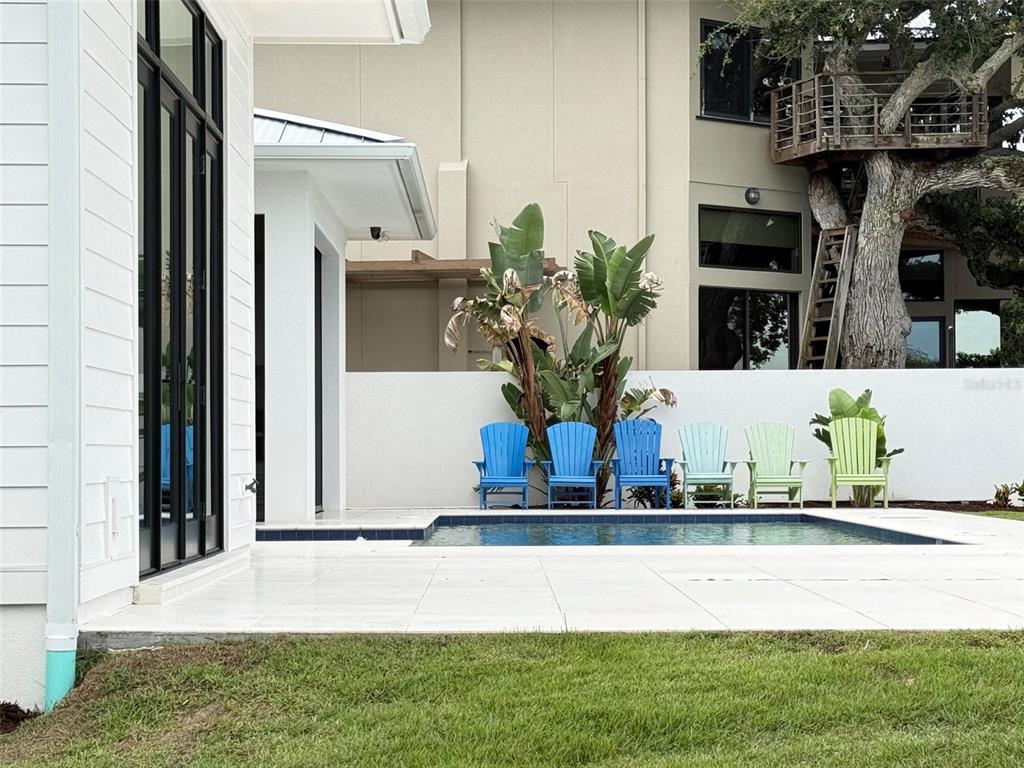 A swimming pool with six colorful Adirondack chairs sits on a patio beside a house — 101 DUE EAST STREET, NEW SMYRNA BEACH, FL